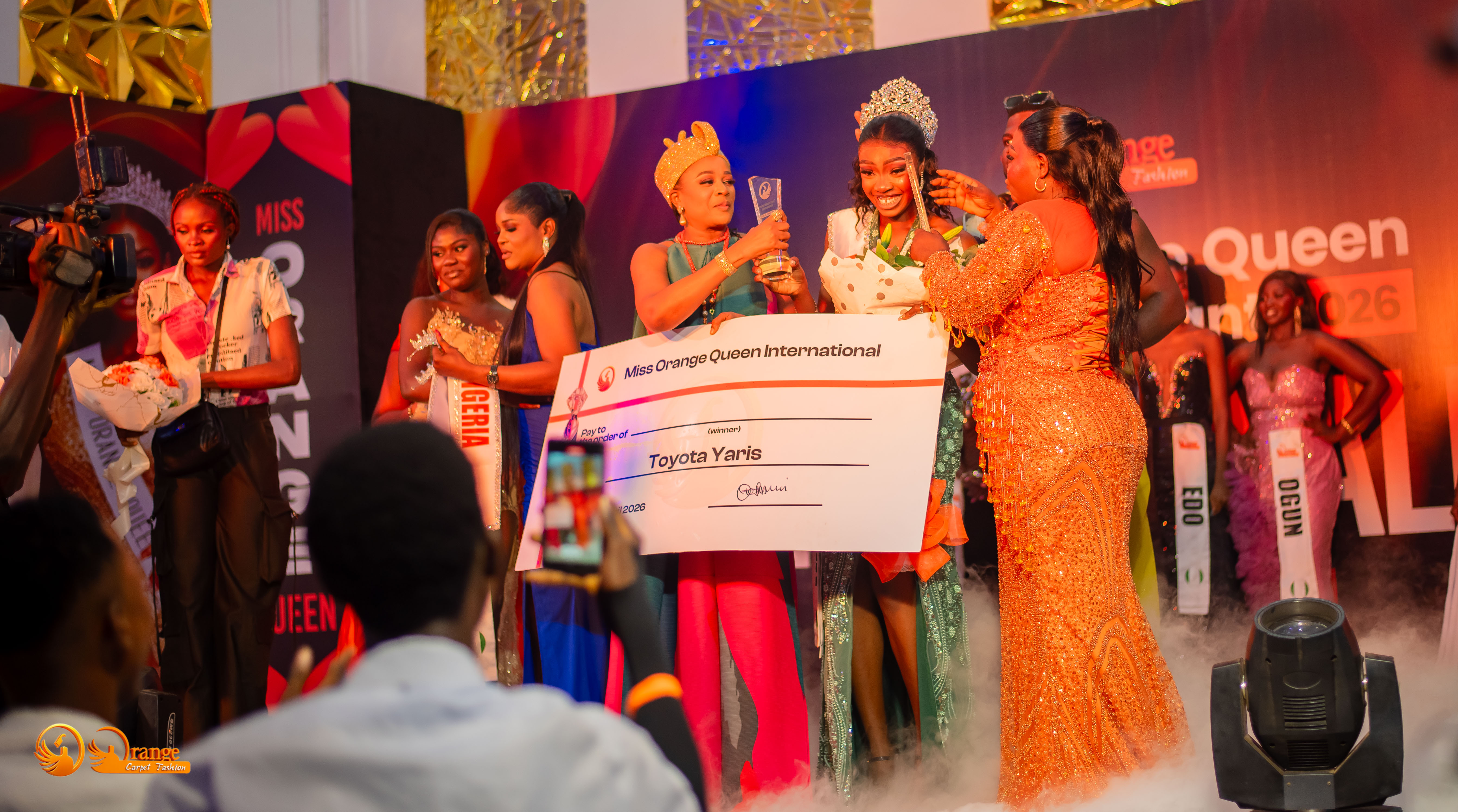 Abigael holding the Toyota Yaris prize cheque with crown and trophy on stage